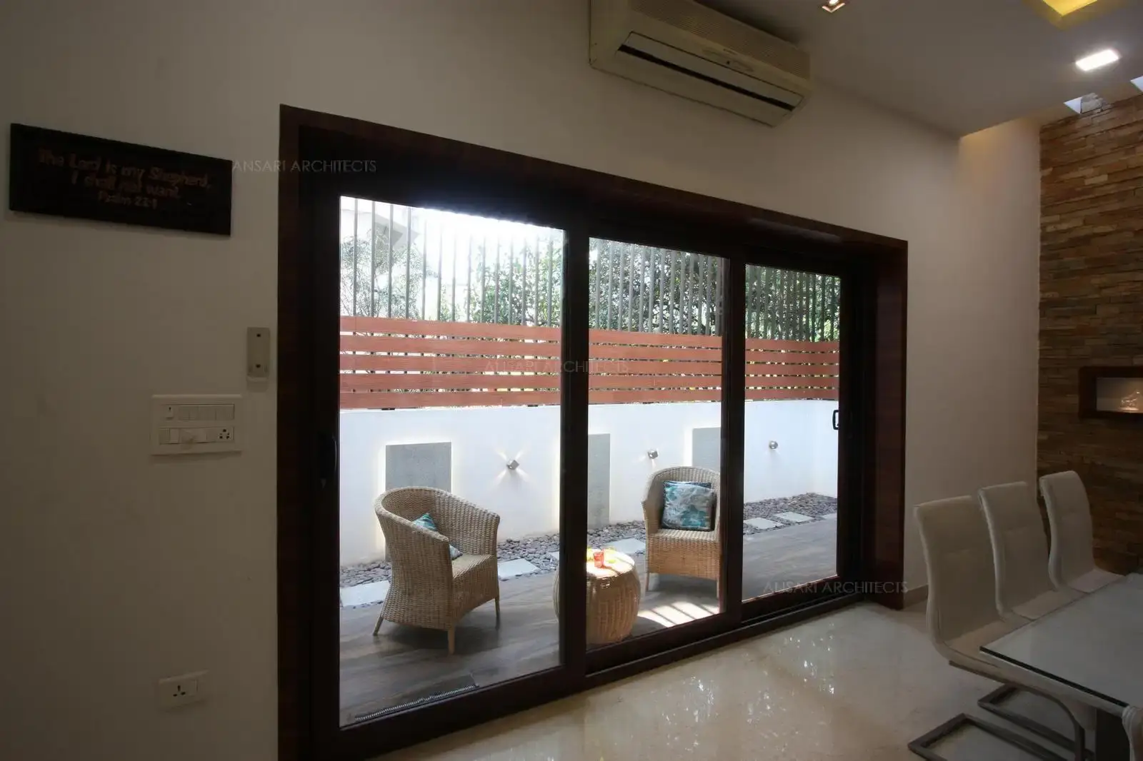 The sliding doors certainly provide openess and fluidity, Courtyard space comprises of wooden flooring in a straight line pattern, infuses an organic warmth into the space along with hardscaping using pebbles and lights enrich the space by where the decor elements are backlit, along with sturdy outdoor furnitures. The deep wood tones provide an earthy backdrop.