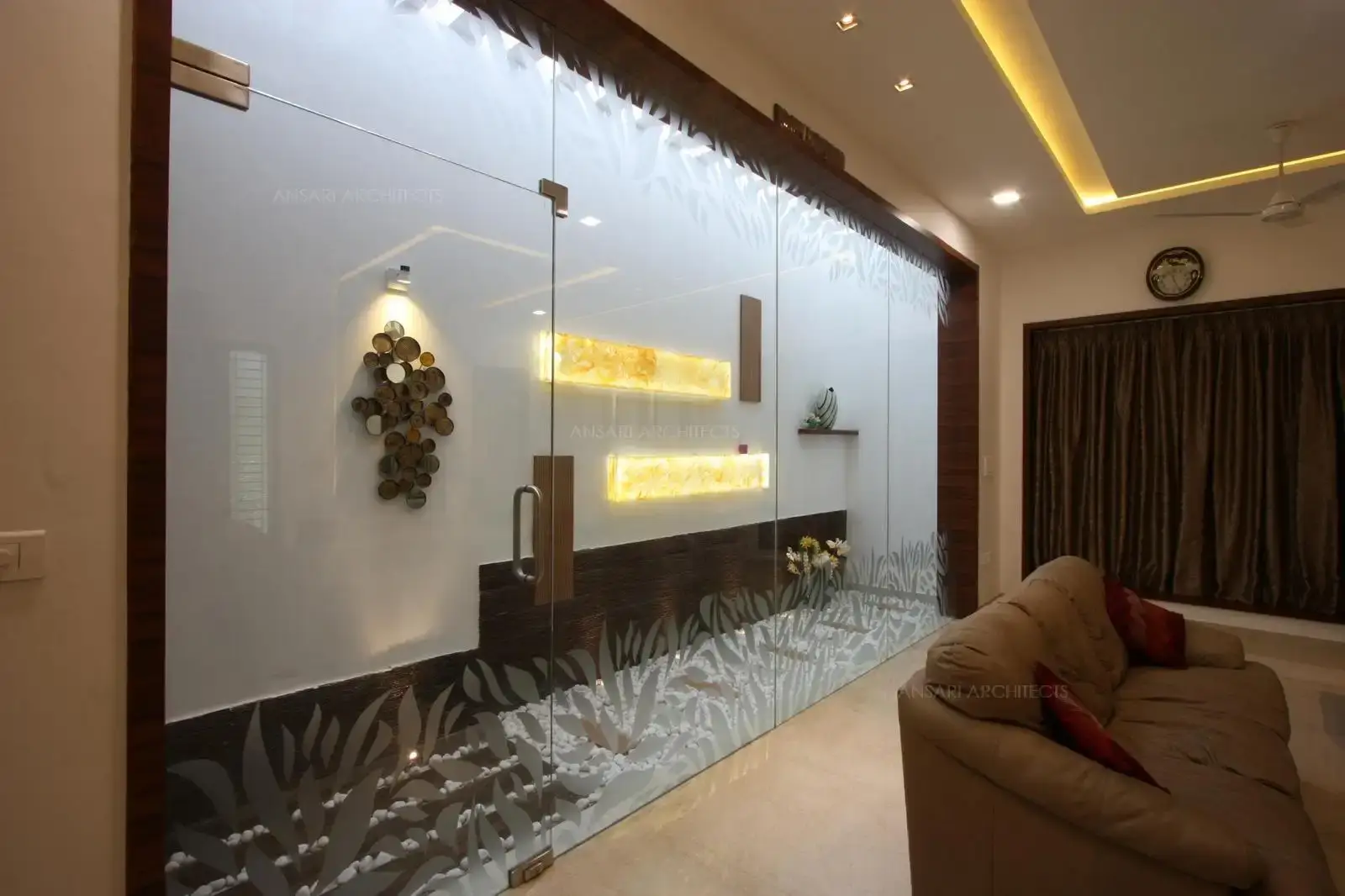 Courtyard is a melange of different materials , textures and tones- the decor elements are highlighted with golden suble lighting and veneer panelling dominates dark tones and hardscaping with pebbles and glass door makes the space a perfect invite spot.