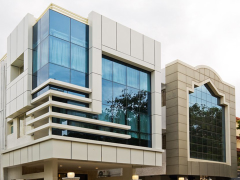 Modern building facade featuring angular white paneling and large reflective blue-tinted glass windows set against a cloudy sky